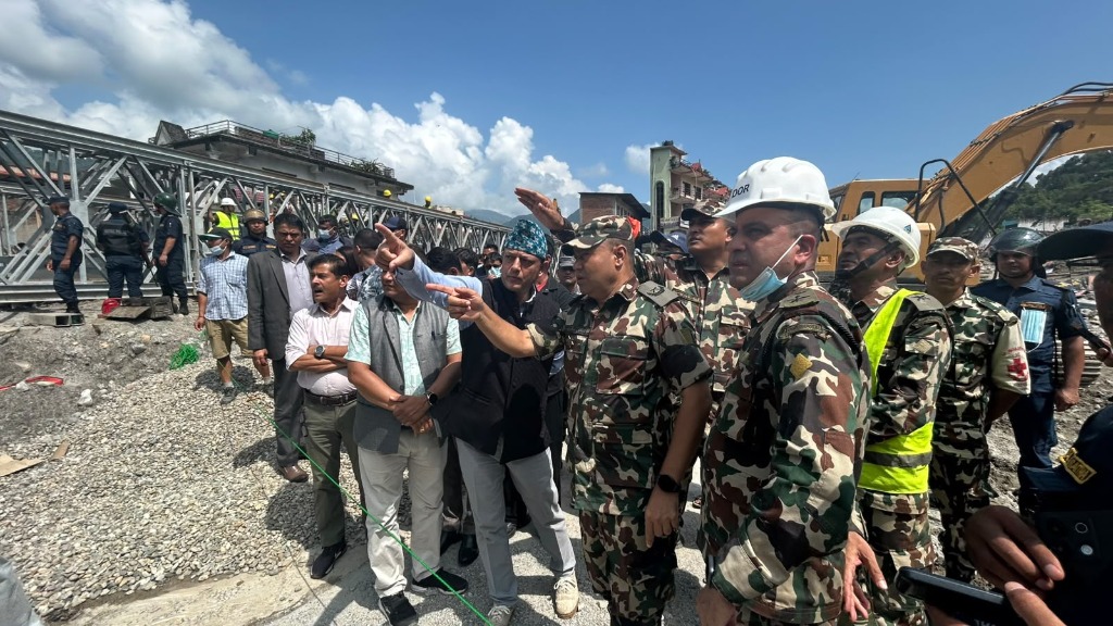 The Speaker of the House of Representatives and military officials surveying flash flood damage alongside heavy machinery and collapsed structures